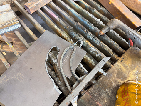 A curve is welded onto a bar. It looks rather phallic. Beneath it, a sheet of steel has been cut with a plasma cutter approximating the curve